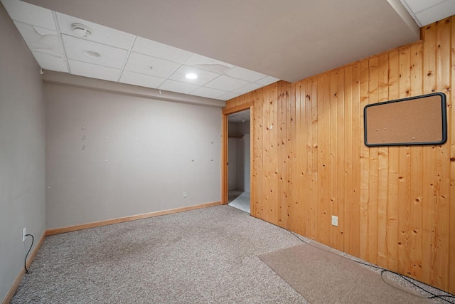 carpeted spare room featuring a drop ceiling and wooden walls