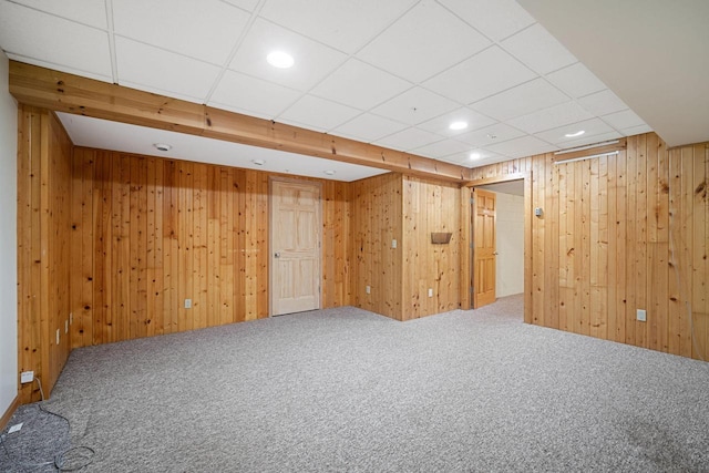 basement with carpet floors, a paneled ceiling, and wooden walls