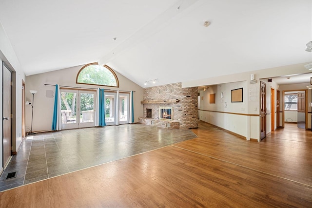 unfurnished living room with beam ceiling, high vaulted ceiling, dark hardwood / wood-style floors, a brick fireplace, and french doors