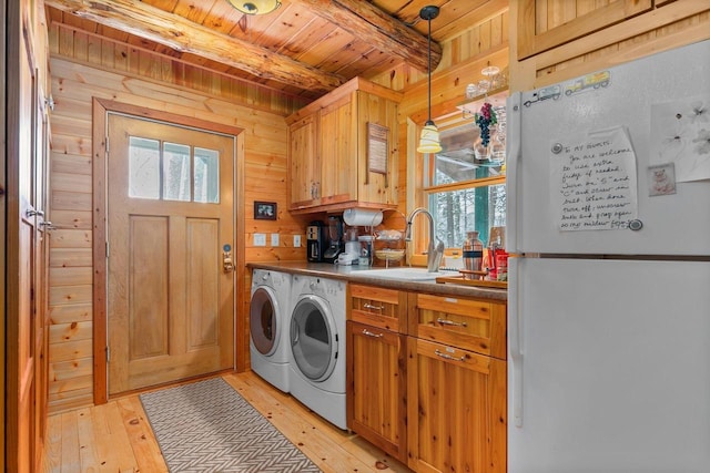 clothes washing area with sink, washing machine and clothes dryer, light wood-type flooring, and wood walls