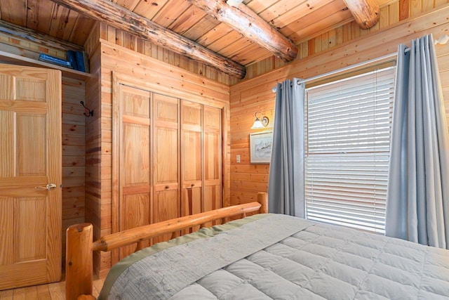 bedroom featuring beam ceiling, wooden ceiling, a closet, and wood walls