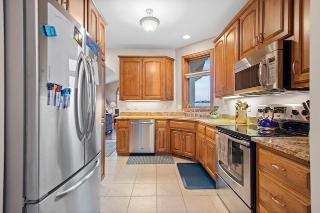 kitchen featuring stainless steel appliances, light stone countertops, sink, and light tile patterned floors