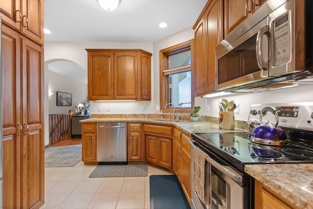 kitchen featuring stainless steel appliances, sink, light tile patterned floors, and light stone counters