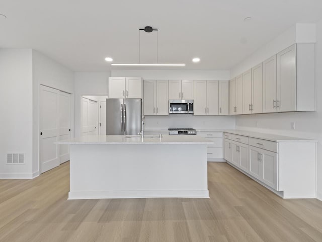 kitchen with appliances with stainless steel finishes, light hardwood / wood-style floors, white cabinets, a center island with sink, and decorative light fixtures