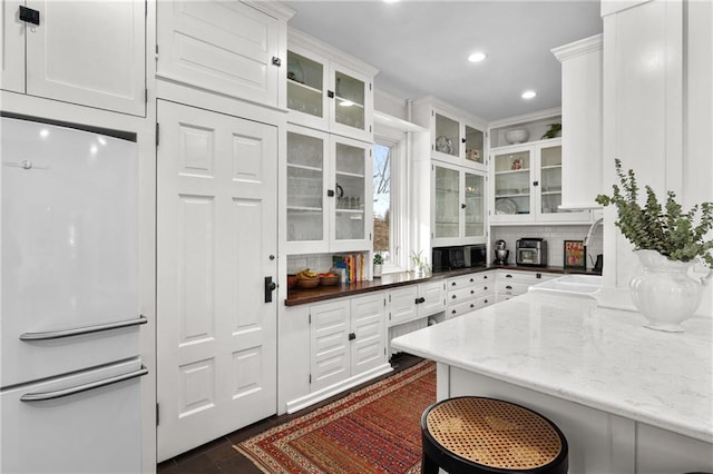 kitchen featuring white cabinetry, dark stone countertops, white refrigerator, a kitchen breakfast bar, and backsplash