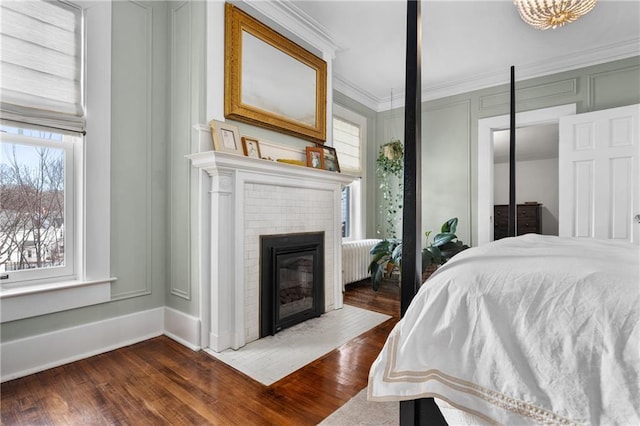 bedroom featuring a fireplace, crown molding, radiator heating unit, and dark hardwood / wood-style floors