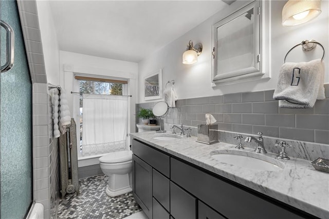 bathroom with vanity, toilet, a shower with shower door, and tile walls