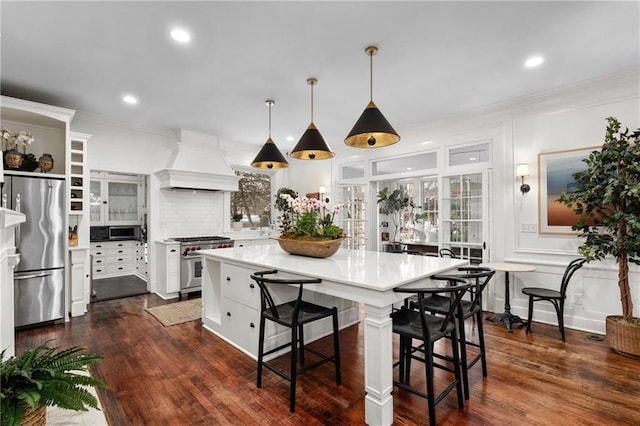 kitchen featuring a breakfast bar area, white cabinetry, hanging light fixtures, appliances with stainless steel finishes, and custom range hood