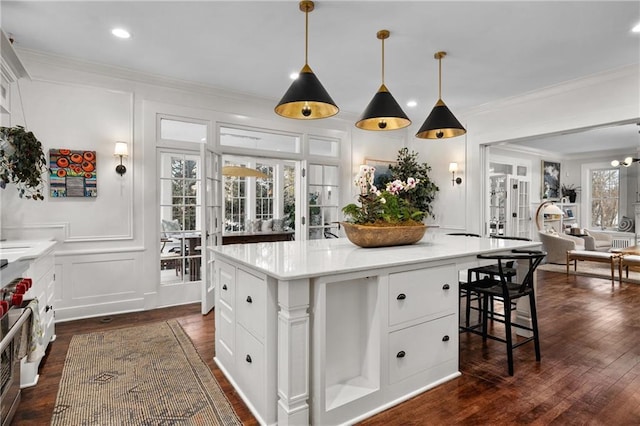 kitchen with white cabinetry, hanging light fixtures, a center island, crown molding, and dark wood-type flooring