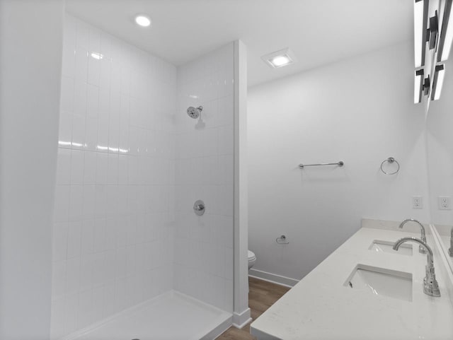 bathroom featuring a tile shower, vanity, wood-type flooring, and toilet