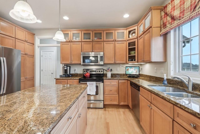 kitchen with appliances with stainless steel finishes, sink, pendant lighting, and light stone counters