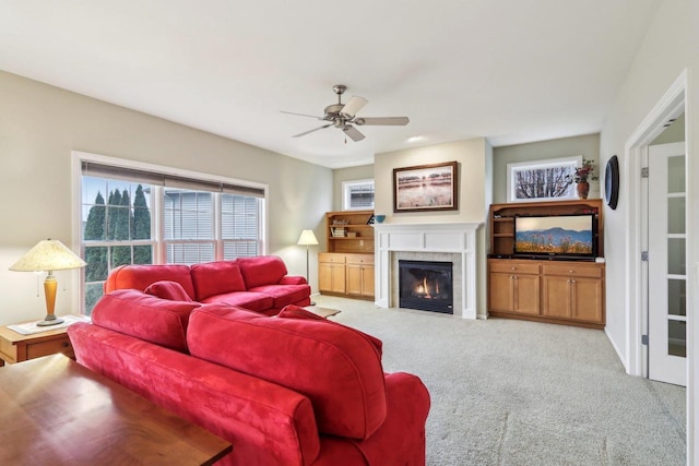 living room with a tiled fireplace, light colored carpet, and ceiling fan