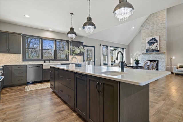 kitchen featuring stainless steel dishwasher, sink, an island with sink, and an inviting chandelier