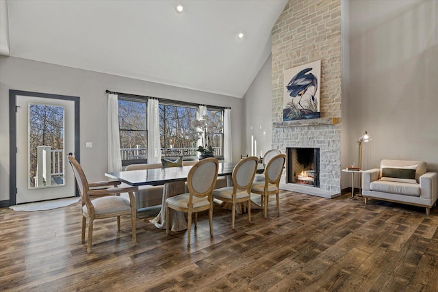 dining area featuring high vaulted ceiling, dark wood-type flooring, and a stone fireplace