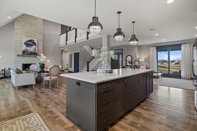 kitchen with dark hardwood / wood-style flooring, a kitchen island with sink, hanging light fixtures, and dark brown cabinetry