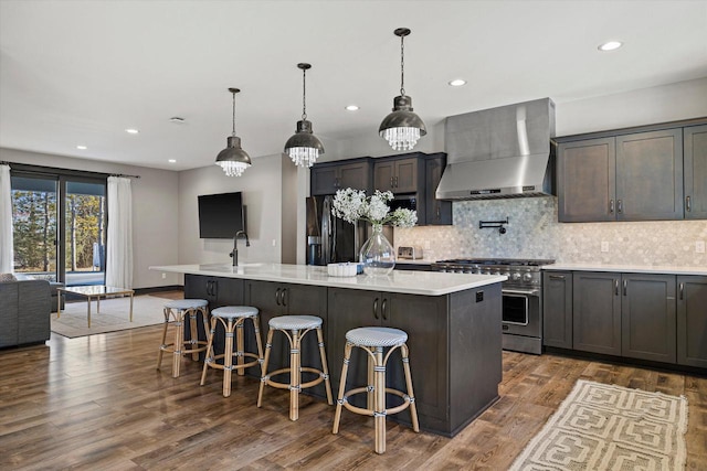 kitchen with a kitchen bar, stainless steel range, decorative light fixtures, wall chimney exhaust hood, and an island with sink