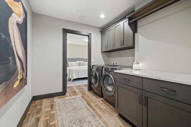 clothes washing area with light wood-type flooring, separate washer and dryer, and cabinets