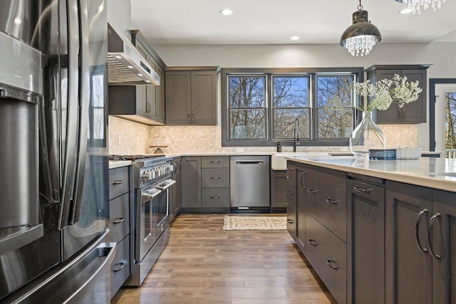 kitchen featuring stainless steel appliances, dark brown cabinetry, dark wood-type flooring, wall chimney range hood, and pendant lighting