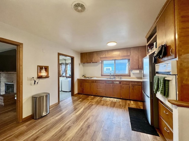 kitchen with sink, light hardwood / wood-style floors, washing machine and dryer, and white oven