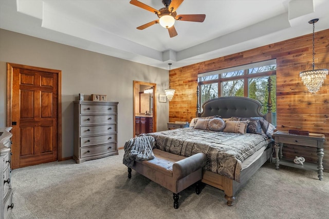 carpeted bedroom with a tray ceiling, wooden walls, and ensuite bathroom