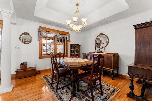 dining room featuring a raised ceiling, a notable chandelier, light hardwood / wood-style floors, and ornate columns