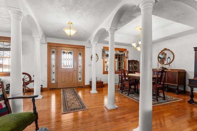 foyer featuring an inviting chandelier, hardwood / wood-style flooring, a textured ceiling, and ornate columns