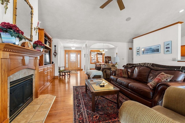 living room featuring ceiling fan with notable chandelier, light hardwood / wood-style flooring, and a tile fireplace