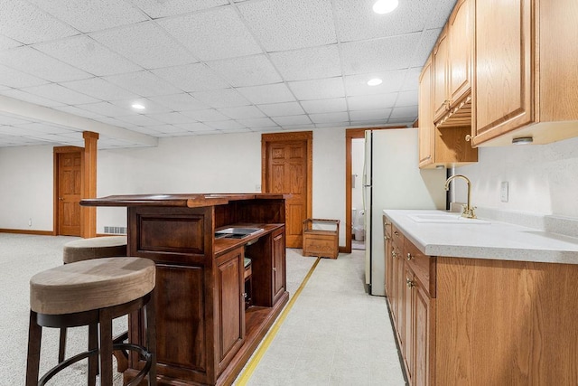 kitchen with white fridge, sink, a paneled ceiling, and a kitchen breakfast bar