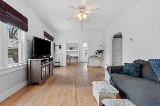 living room featuring built in shelves, light hardwood / wood-style flooring, and ceiling fan