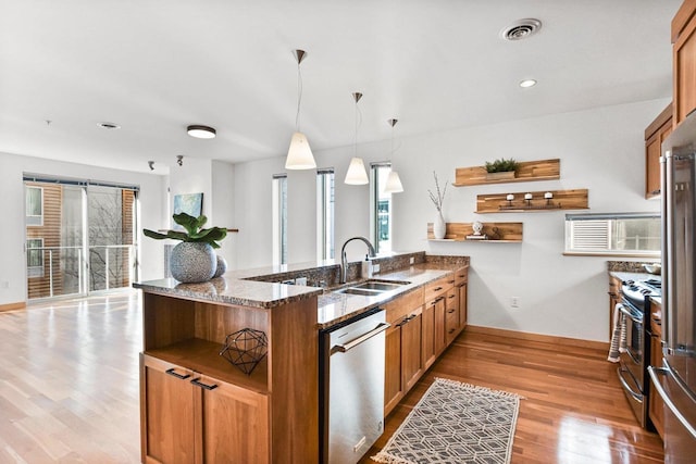 kitchen with appliances with stainless steel finishes, a wealth of natural light, decorative light fixtures, light stone counters, and kitchen peninsula