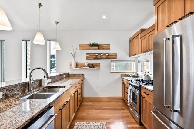 kitchen with appliances with stainless steel finishes, sink, hanging light fixtures, and dark stone counters