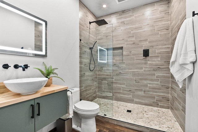 bathroom with a tile shower, vanity, hardwood / wood-style flooring, and toilet