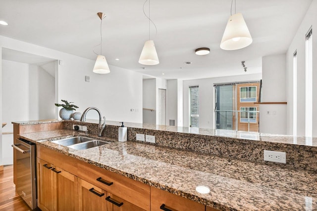 kitchen featuring sink, stainless steel dishwasher, light stone countertops, and hanging light fixtures