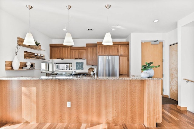 kitchen featuring light stone counters, stainless steel fridge, kitchen peninsula, and wood-type flooring