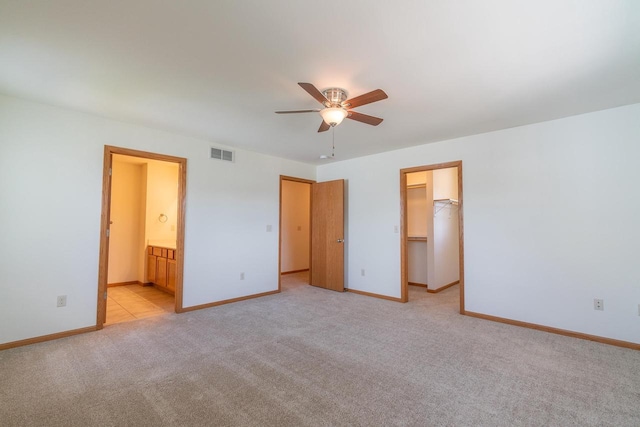 unfurnished bedroom featuring connected bathroom, a walk in closet, light carpet, a closet, and ceiling fan