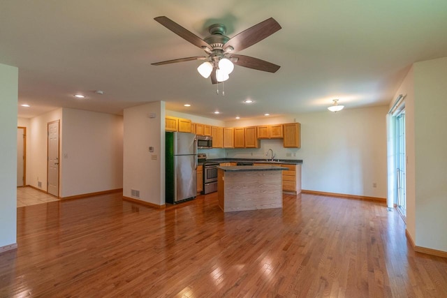 kitchen featuring light brown cabinetry, a kitchen island, ceiling fan, stainless steel appliances, and light hardwood / wood-style floors