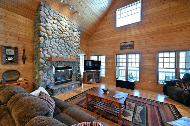 living room with hardwood / wood-style flooring, a stone fireplace, plenty of natural light, and wooden walls