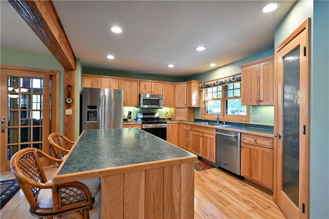 kitchen with a kitchen island, appliances with stainless steel finishes, a breakfast bar, sink, and light hardwood / wood-style floors