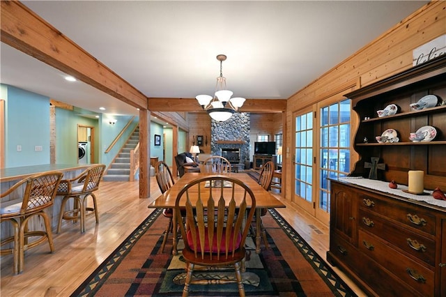 dining area featuring beam ceiling, a notable chandelier, a fireplace, light hardwood / wood-style floors, and french doors