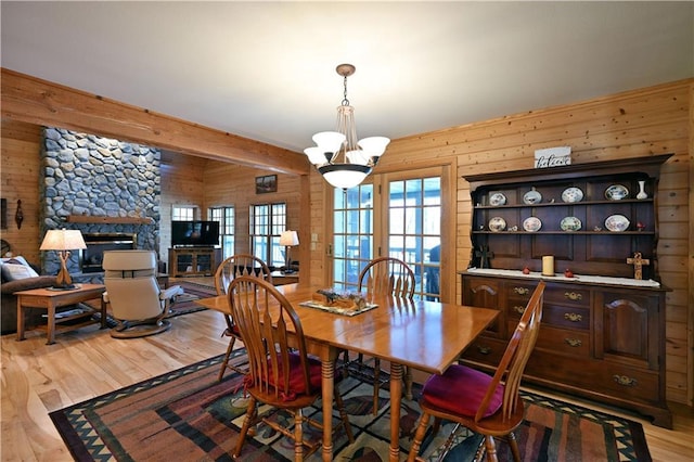 dining space featuring a stone fireplace, light hardwood / wood-style floors, and wood walls