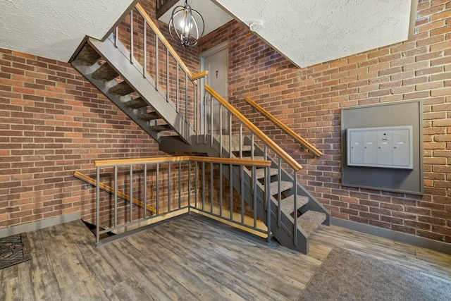 staircase featuring hardwood / wood-style floors, a mail area, a textured ceiling, and brick wall