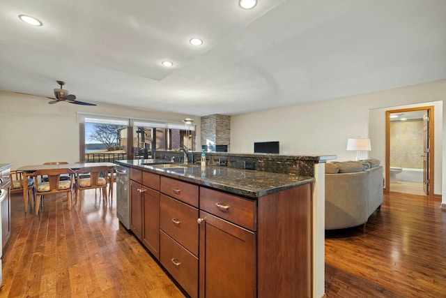 kitchen with sink, dark hardwood / wood-style floors, dishwasher, an island with sink, and dark stone counters