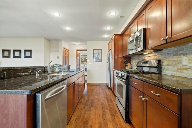 kitchen featuring sink, appliances with stainless steel finishes, backsplash, wood-type flooring, and dark stone counters