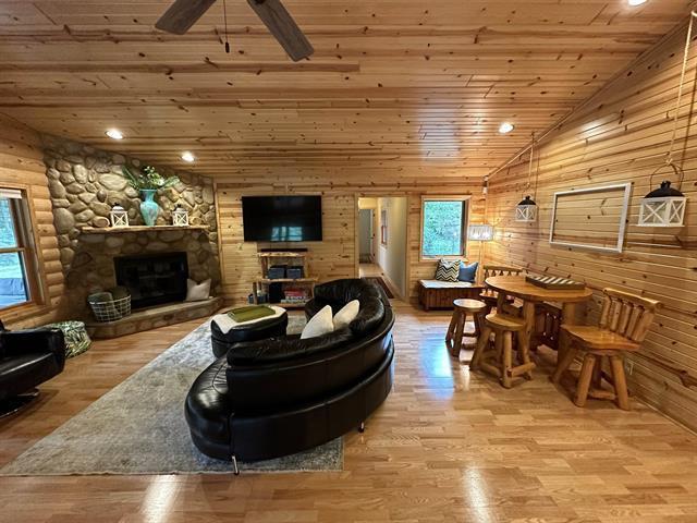 living room with vaulted ceiling, light wood-type flooring, wooden ceiling, ceiling fan, and a fireplace