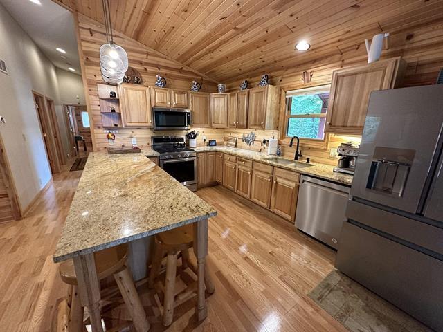 kitchen with pendant lighting, sink, a breakfast bar area, stainless steel appliances, and light wood-type flooring