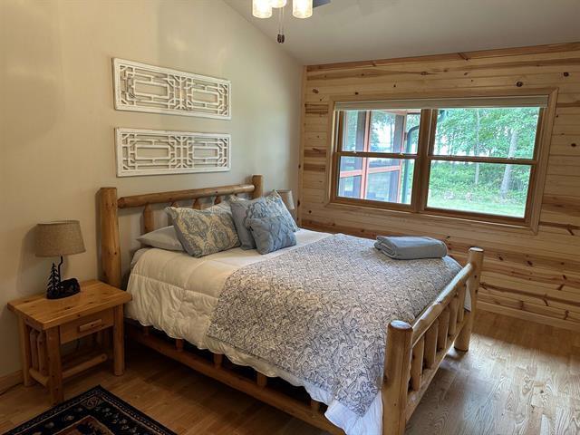 bedroom with lofted ceiling, hardwood / wood-style floors, and wooden walls