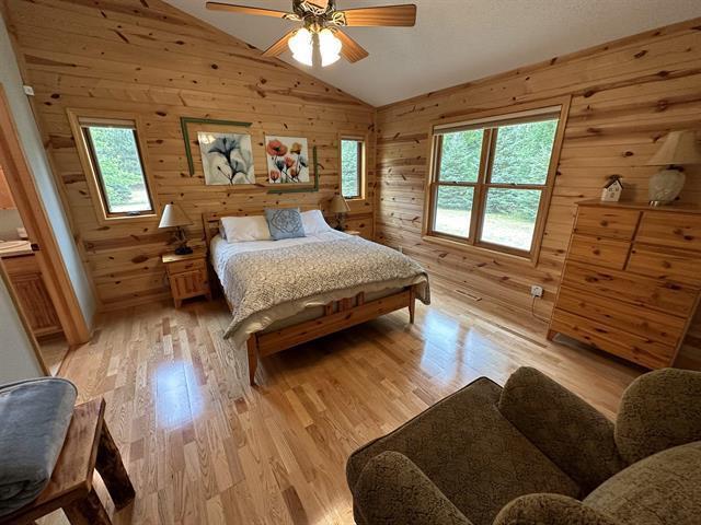 bedroom with multiple windows, light hardwood / wood-style flooring, wood walls, and vaulted ceiling