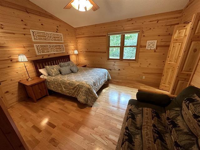 bedroom featuring ceiling fan, wooden walls, light hardwood / wood-style floors, and vaulted ceiling