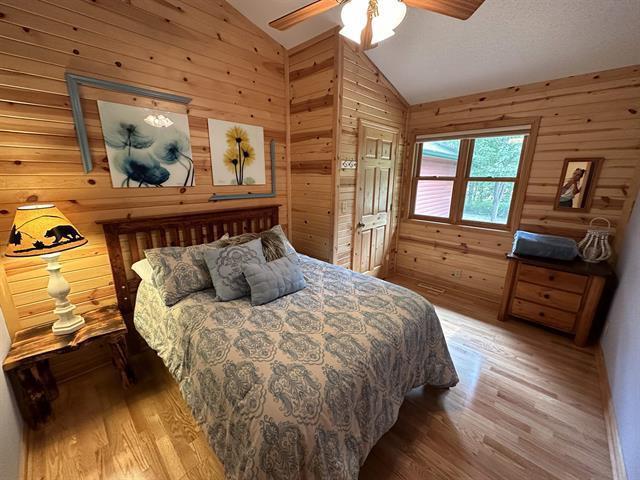 bedroom with ceiling fan, lofted ceiling, hardwood / wood-style floors, and wood walls