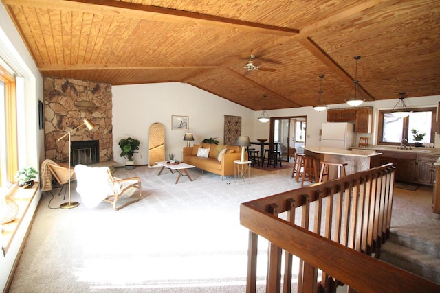 carpeted living room with lofted ceiling, a stone fireplace, sink, and wooden ceiling